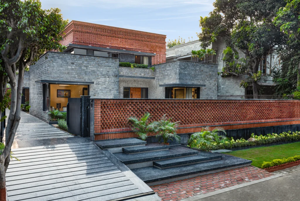 Modern house with gray stone and red brick walls, black gate, landscaped yard, and large windows.