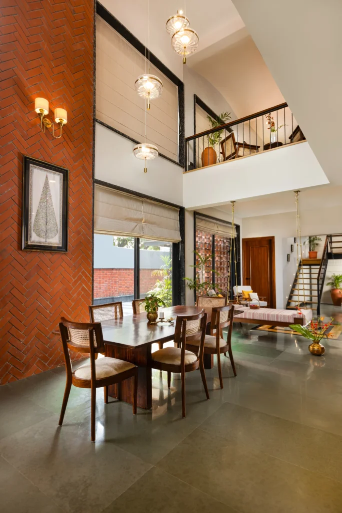 Spacious dining and living area with wooden table, chairs, brick wall, hanging lights, and staircase.