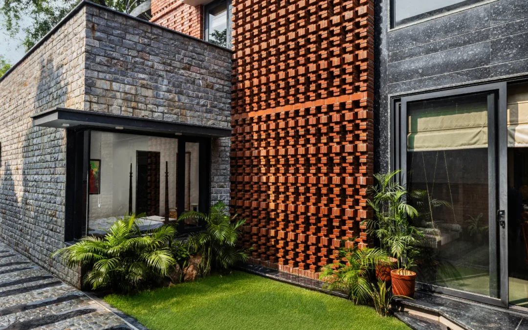 Modern building exterior with textured brick wall, stone facade, glass doors, and green lawn.