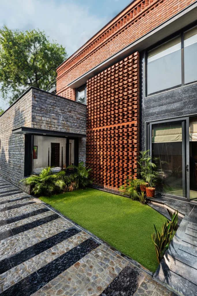 Modern building exterior with textured brick wall, stone facade, glass doors, and green lawn.